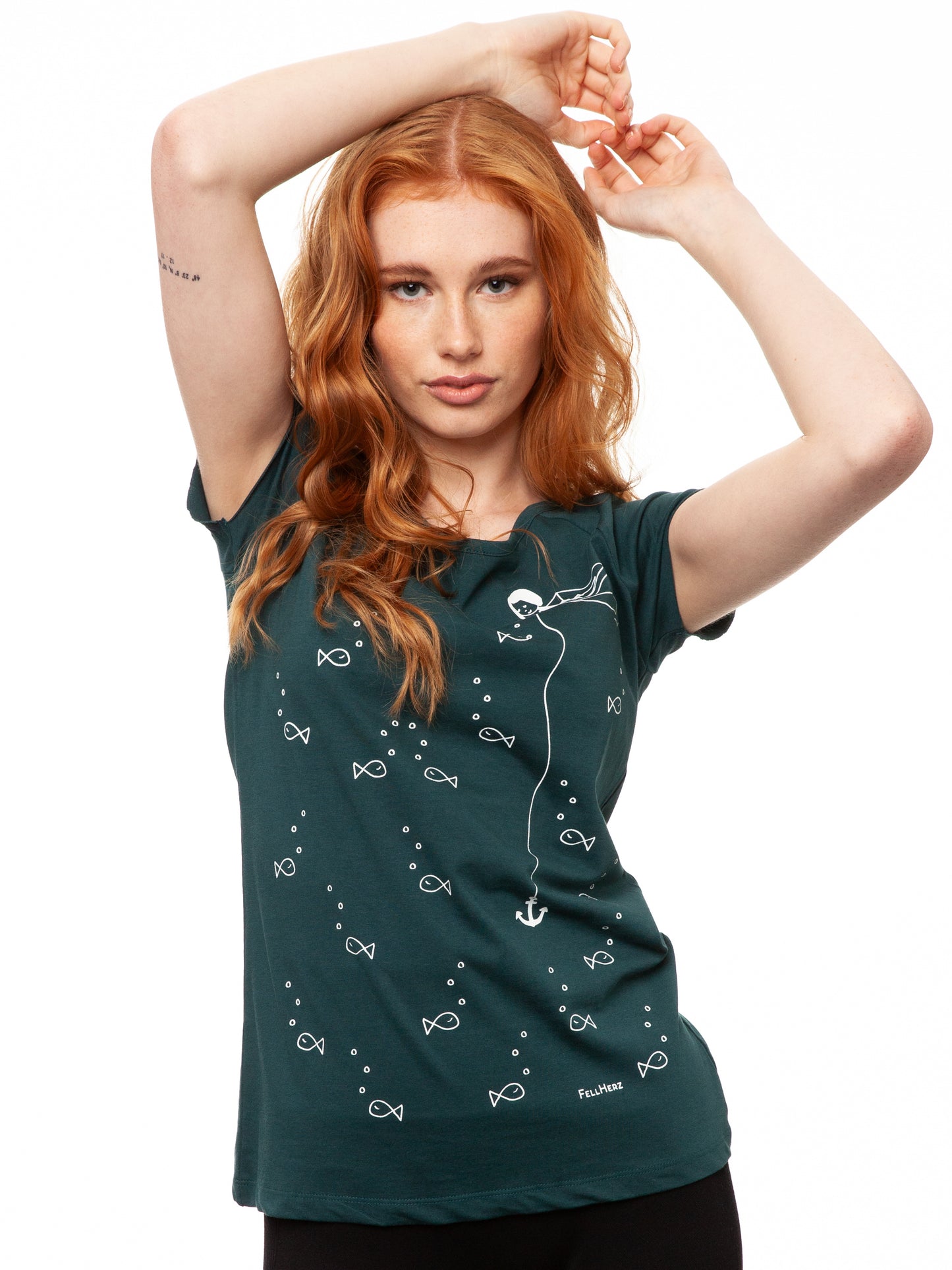 Ein Model trägt ein petrolfarbens Damen T‑Shirt aus 100 % Bio‑Baumwolle mit kurzen Cap‑Sleeves, maritimem Anker‑Siebdruck vorne und kleinem Logo‑Print auf dem Rücken – nachhaltig, fair produziert und lässig geschnitten