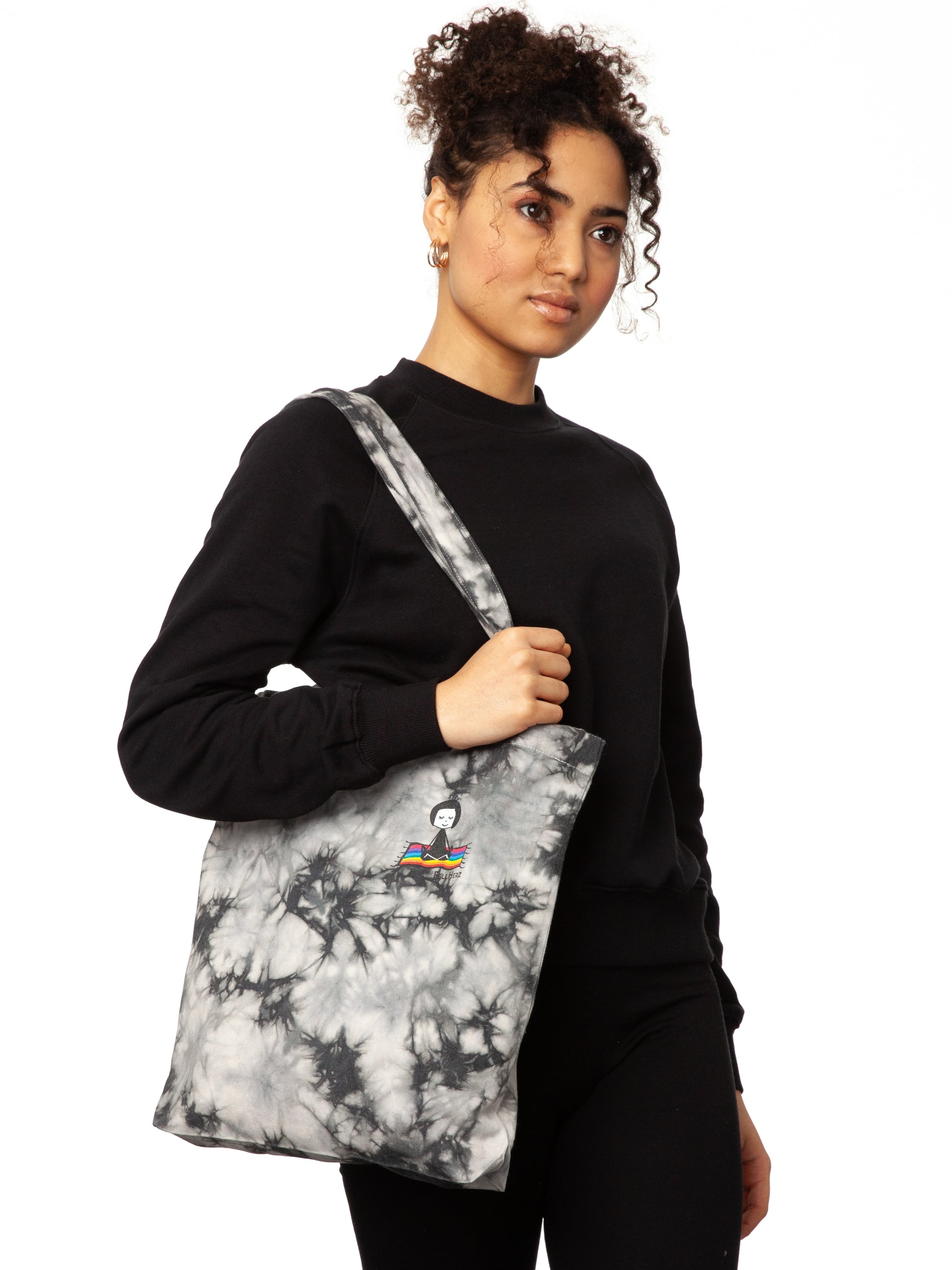 Schwarz weiße Batik‑Tote‑Bag ‘Ommm’ in handgefärbtem Tie‑Dye‑Muster, ca. 37 × 39 cm, aus 300 g/m² Canvas (80 % recycelte Baumwolle, 20 % recycelter Polyester), mit robust verstärkten Kanten, extra Volumen durch Bodennaht und digitalem Ommm‑Print, auf dem ein Mädchen auf einem regenbogenfarbenen Teppich fliegt – fair produziert (Fair Wear), vorgewaschen, waschbar bei 30 °C