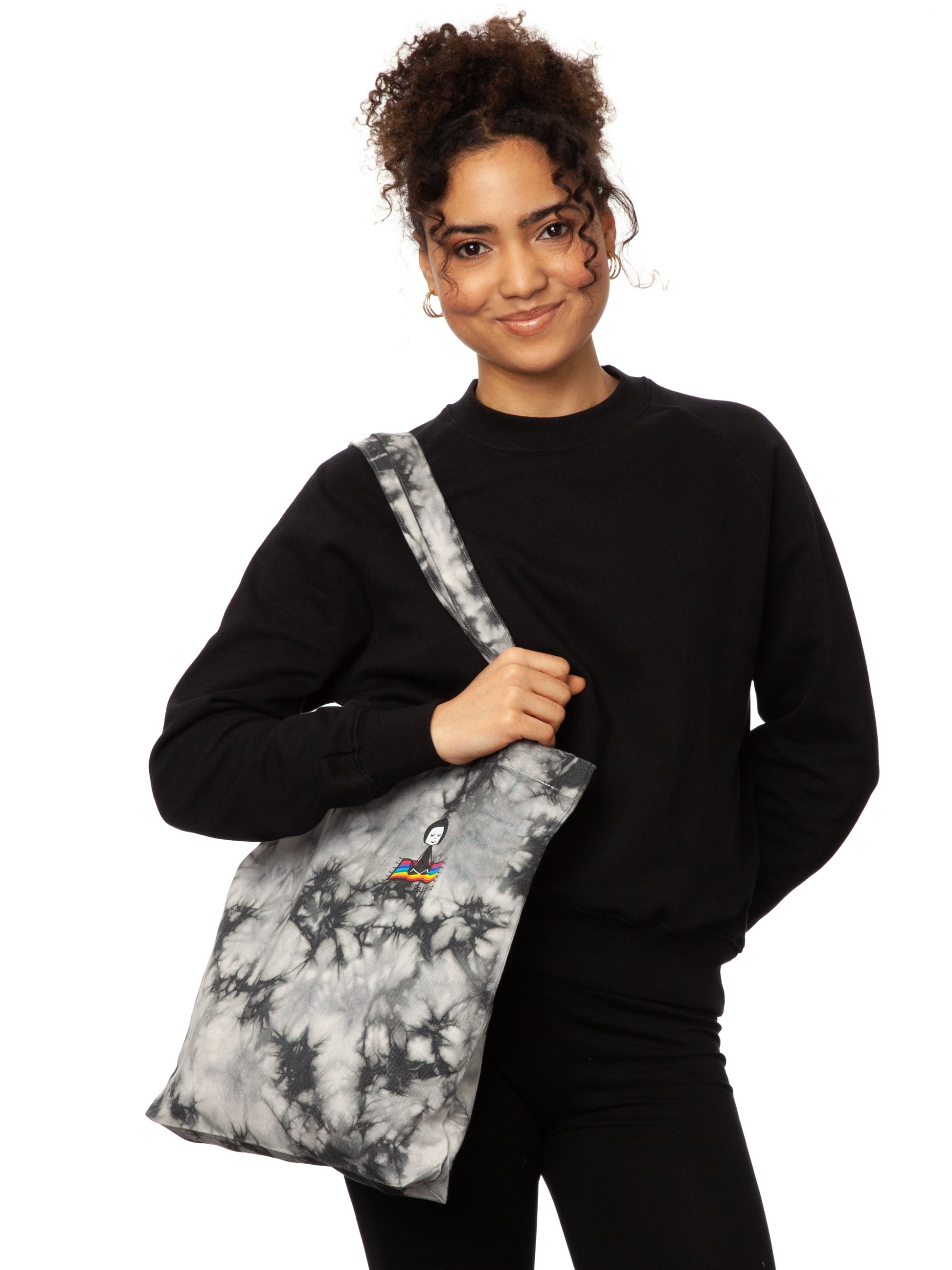 Schwarz weiße Batik‑Tote‑Bag ‘Ommm’ in handgefärbtem Tie‑Dye‑Muster, ca. 37 × 39 cm, aus 300 g/m² Canvas (80 % recycelte Baumwolle, 20 % recycelter Polyester), mit robust verstärkten Kanten, extra Volumen durch Bodennaht und digitalem Ommm‑Print, auf dem ein Mädchen auf einem regenbogenfarbenen Teppich fliegt – fair produziert (Fair Wear), vorgewaschen, waschbar bei 30 °C