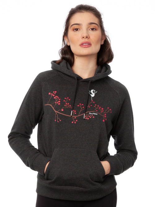 Dunkelgrauer Kapuzenpullover im Raglanschnitt mit Kängurutasche und doppellagiger Kapuze. Der Hoodie besteht aus 85 % Biobaumwolle und 15 % recyceltem Polyester. Auf der Vorderseite ist eine stilisierte Yoga-Girl-Illustration, ein Mädchen steht auf einem braunen Zweig mit pinken Beeren in einer Balance-Yoga-Pose in sanften Farben auf Wasserbasis digital gedruckt