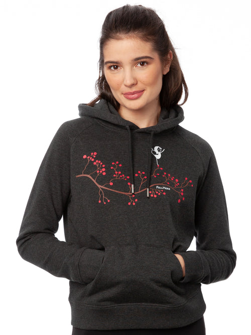 Dunkelgrauer Kapuzenpullover im Raglanschnitt mit Kängurutasche und doppellagiger Kapuze. Der Hoodie besteht aus 85 % Biobaumwolle und 15 % recyceltem Polyester. Auf der Vorderseite ist eine stilisierte Yoga-Girl-Illustration, ein Mädchen steht auf einem braunen Zweig mit pinken Beeren in einer Balance-Yoga-Pose in sanften Farben auf Wasserbasis digital gedruckt