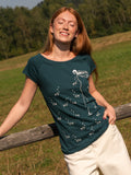 Ein Model trägt ein Damen T‑Shirt deep teal aus 100 % Bio‑Baumwolle mit kurzen Cap‑Sleeves, maritimem Anker‑Siebdruck vorne und kleinem Logo‑Print auf dem Rücken – nachhaltig, fair produziert und lässig geschnitten