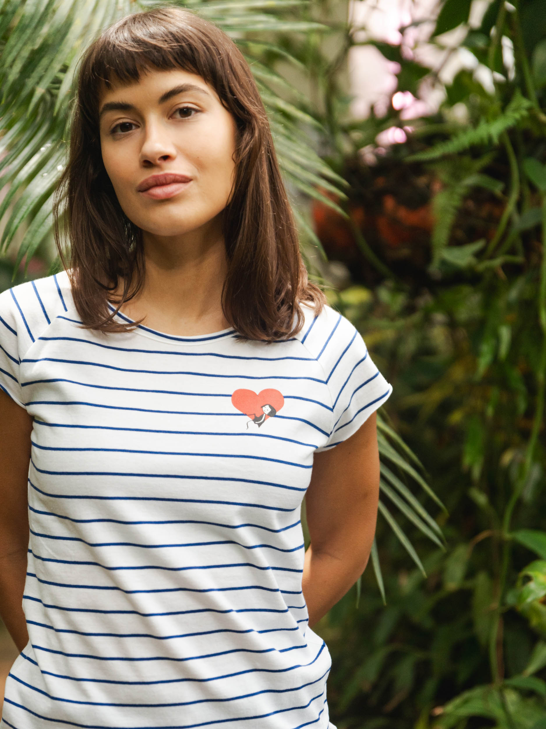 Ein Model trägt ein blau weiß gestreiftes Damen T-Shirt aus Bio-Baumwolle, fair und vegan produziert. Das Raglan-Shirt hat einen Grafik-Print auf der Vorderseite: Ein Herz in dem ein kleines Mädche sitzt. Der Druck ist mit wasserbasierenden Farben ohne Schadstoffe gedruckt.