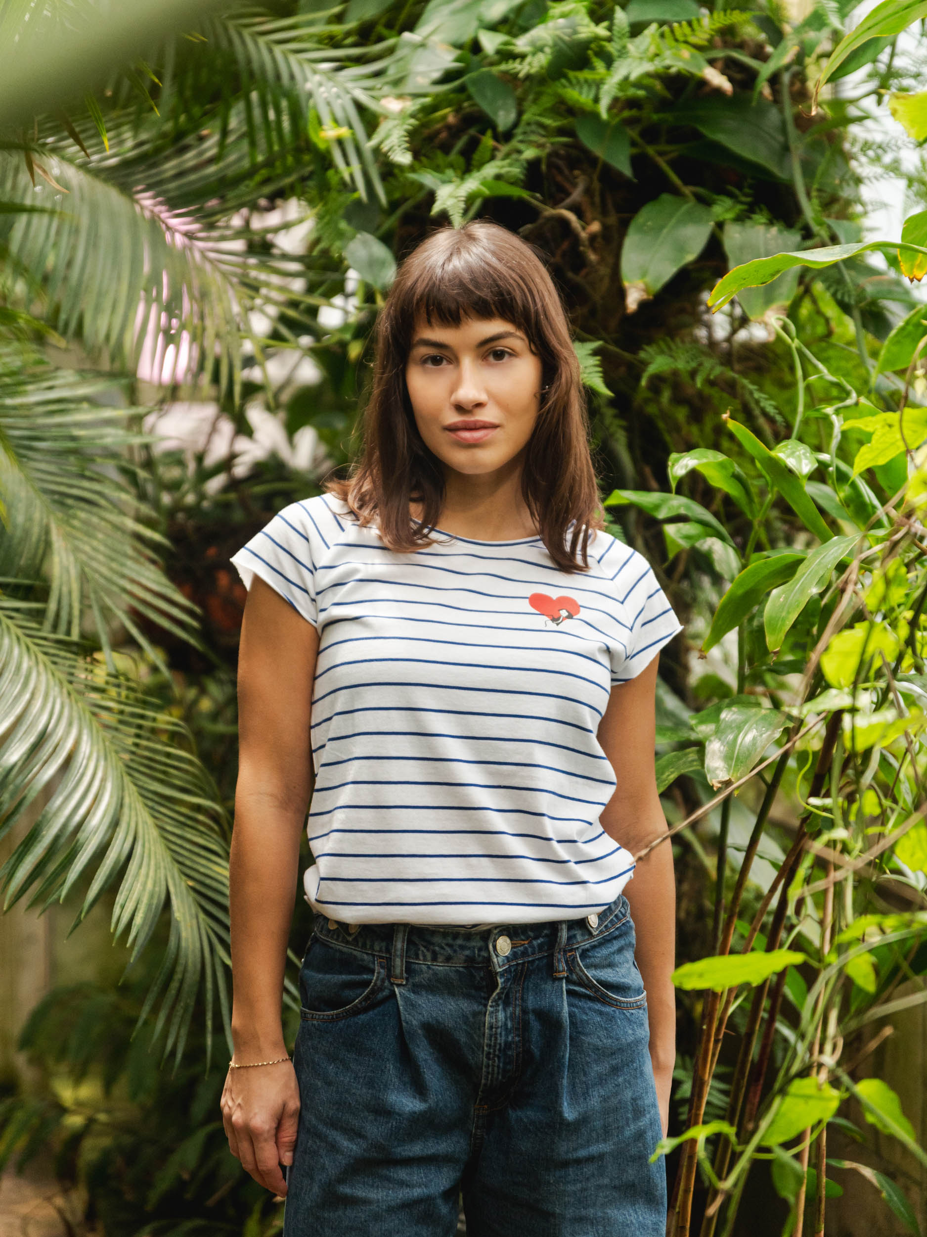 Ein Model trägt ein blau weiß gestreiftes Damen T-Shirt aus Bio-Baumwolle, fair und vegan produziert. Das Raglan-Shirt hat einen Grafik-Print auf der Vorderseite: Ein Herz in dem ein kleines Mädche sitzt. Der Druck ist mit wasserbasierenden Farben ohne Schadstoffe gedruckt.