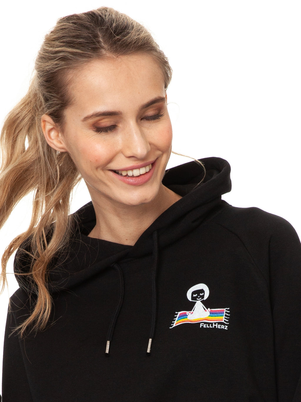 Schwarzer Ommm‑Hoodie aus 85 % Bio‑Baumwolle und 15 % recyceltem Polyester im lässigen Raglan‑Schnitt, mit doppellagiger Kapuze und Ton‑in‑Ton‑Kordel, kuscheliger Kängurutasche und zarter FellHerz‑Illustration eines kleinen Mädchens, das auf einem regenbogenfarbenen Teppich fliegt, im Digitaldruck mit wasserbasierten Farben – nachhaltig, fair produziert und ideal für kalte Tage.