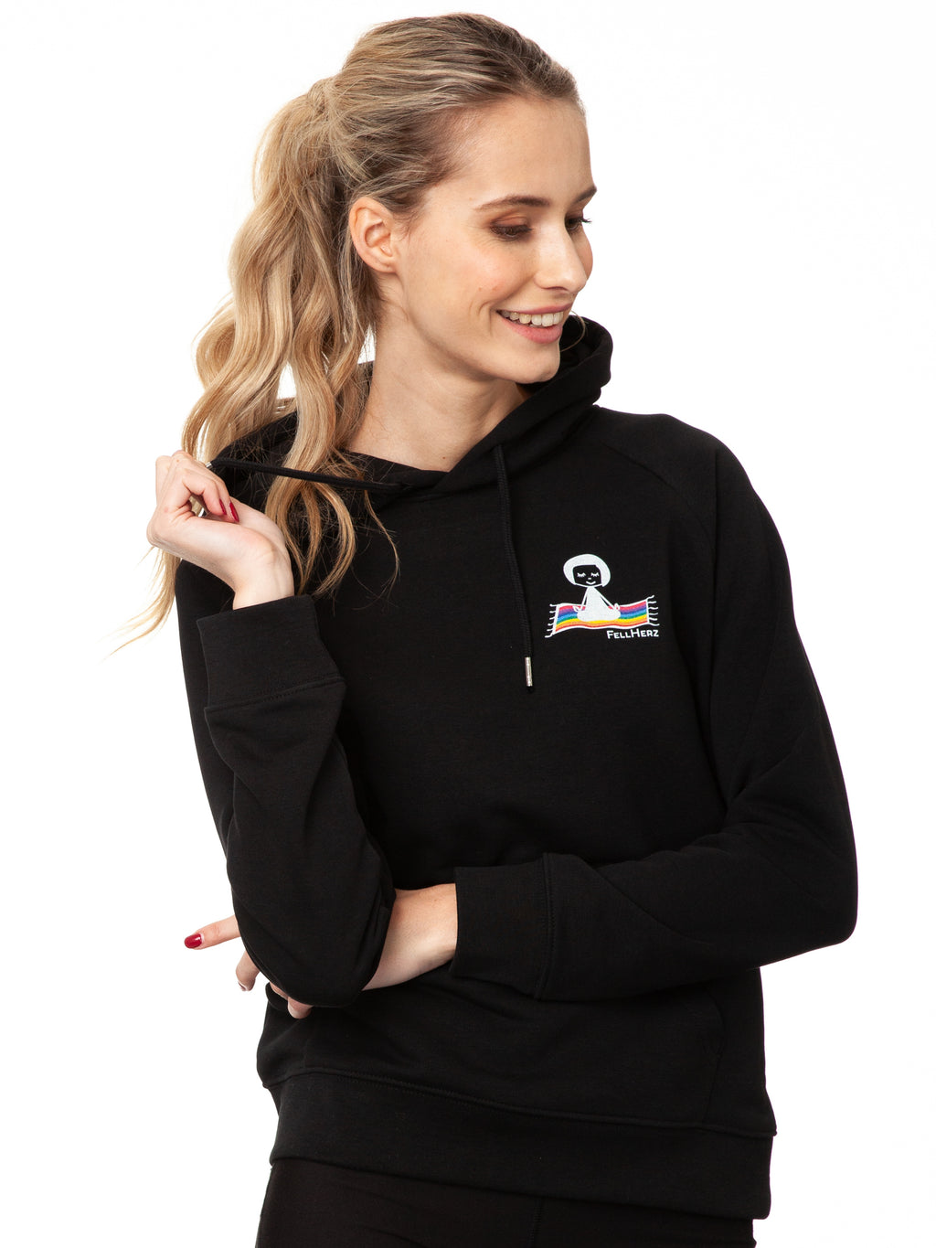 Schwarzer Ommm‑Hoodie aus 85 % Bio‑Baumwolle und 15 % recyceltem Polyester im lässigen Raglan‑Schnitt, mit doppellagiger Kapuze und Ton‑in‑Ton‑Kordel, kuscheliger Kängurutasche und zarter FellHerz‑Illustration eines kleinen Mädchens, das auf einem regenbogenfarbenen Teppich fliegt, im Digitaldruck mit wasserbasierten Farben – nachhaltig, fair produziert und ideal für kalte Tage.