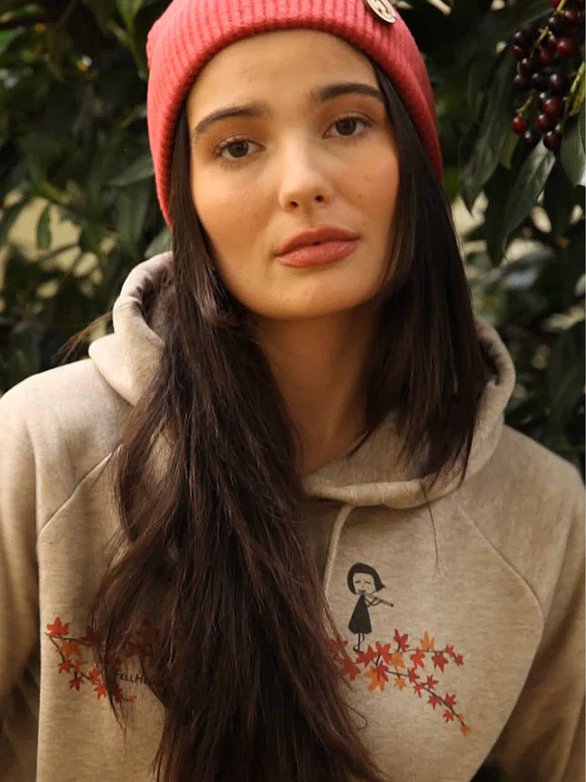 Ein weibliches Model trägt einen FellHerz Hoodie in heather sand. Der Druck auf dem Hoodie zeigt ein kleines Mädchen, das Querflöte spielt und über einen Ast mit Ahornblättern läuft.