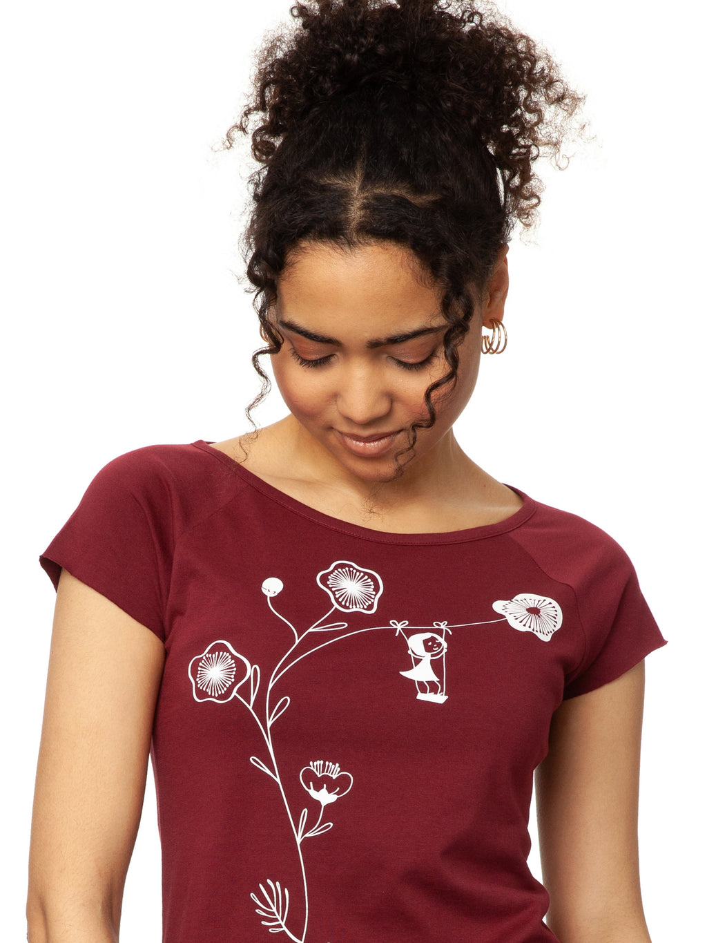 Ein Damen-T-Shirt in kräftigem Rubinrot mit kurzen Cap-Ärmeln. Auf der Vorderseite ist ein filigranes Siebdruck-Motiv eines Mädchens auf einer Schaukel zu sehen, die an einem Kirschblüten Zweig hängt. Das T-Shirt hat eine leicht taillierte Passform und besteht aus weicher Bio-Baumwolle und ist nachhaltig und fair produziert.