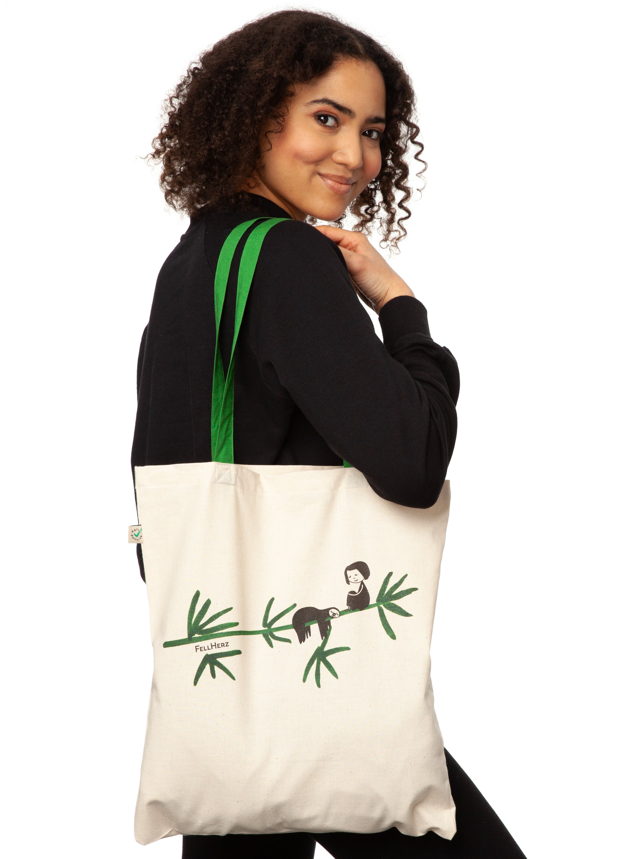 Tasche aus hochwertiger Bio-Baumwolle in Naturweiß mit grünen Henkeln mit einzigartigen FellHerz Faultier-Design in Grün auf der Vorderseite. Die liebevolle Illustration zeigt ein entspanntes Faultier, das sich an einem Zweig festhält, während ein kleines Mädchen daneben sitzt. Diese nachhaltige Bag ist ideal für umweltbewusste Modefans und Fair Fashion Liebhaberinnen und ist ein tolles Accessoire.