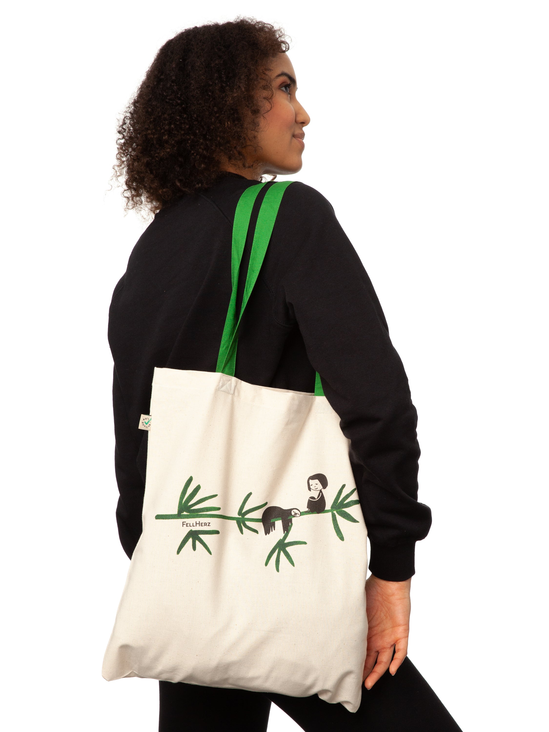 Tasche aus hochwertiger Bio-Baumwolle in Naturweiß mit grünen Henkeln mit einzigartigen FellHerz Faultier-Design in Grün auf der Vorderseite. Die liebevolle Illustration zeigt ein entspanntes Faultier, das sich an einem Zweig festhält, während ein kleines Mädchen daneben sitzt. Diese nachhaltige Bag ist ideal für umweltbewusste Modefans und Fair Fashion Liebhaberinnen und ist ein tolles Accessoire.
