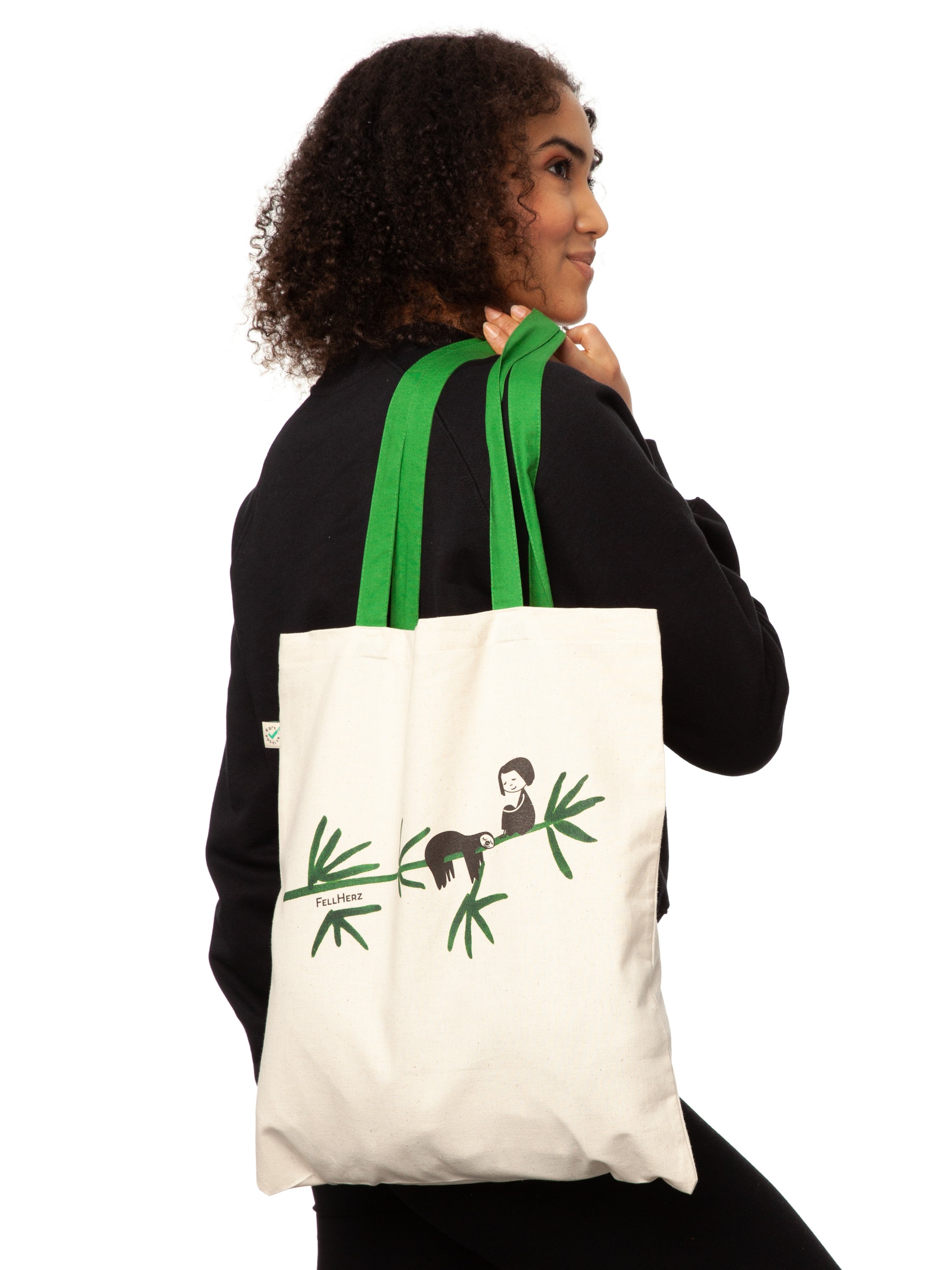 Tasche aus hochwertiger Bio-Baumwolle in Naturweiß mit grünen Henkeln mit einzigartigen FellHerz Faultier-Design in Grün auf der Vorderseite. Die liebevolle Illustration zeigt ein entspanntes Faultier, das sich an einem Zweig festhält, während ein kleines Mädchen daneben sitzt. Diese nachhaltige Bag ist ideal für umweltbewusste Modefans und Fair Fashion Liebhaberinnen und ist ein tolles Accessoire.