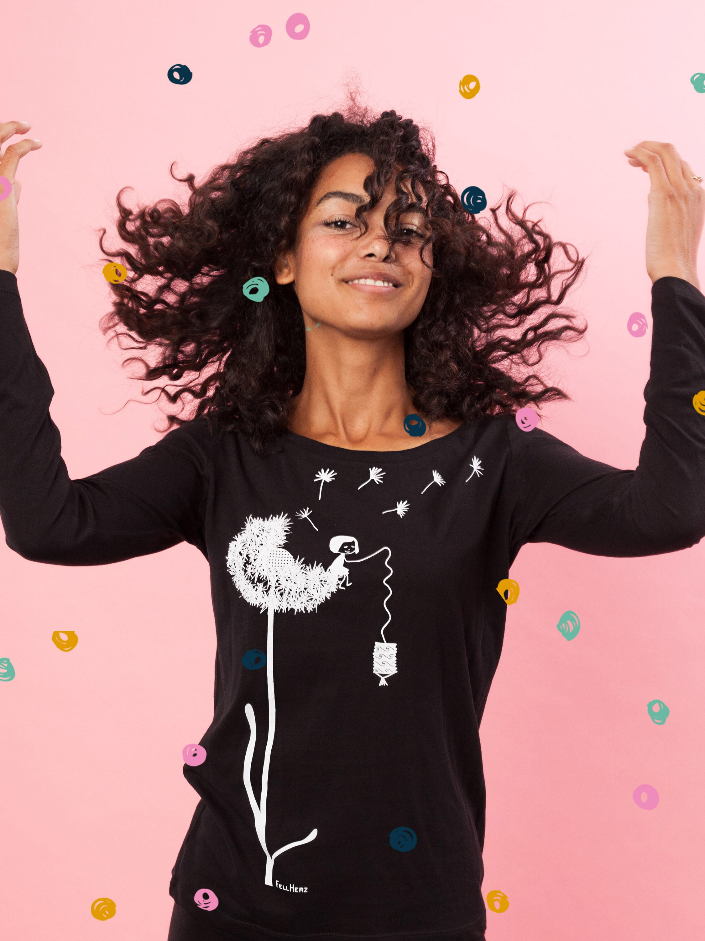 Das Damen Langarm-Shirt in Schwarz besticht durch sein kreatives, weißes FellHerz-Pusteblumen-Print-Design auf der Vorderseite. Die Illustration zeigt ein Mädchen, das mit einer Laterne auf der Blume sitzt. Pusteblumen Samen fliegen davon. Das leicht taillierte Longsleeve hat einen weiten Rundhalsausschnitt, besteht aus weicher, nachhaltiger Bio-Baumwolle und ist fair und vegan produziert. 